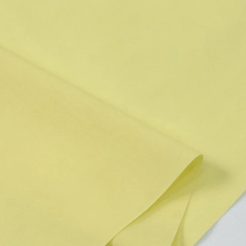 Un gros plan de Popeline polyester-coton au mètre de Longan Craft France en jaune clair, soigneusement plié, met en valeur ce doux et respirant tissu popeline uni-idéal pour robes, chemises et langes.