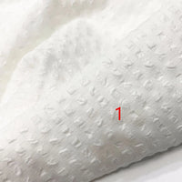 Gros plan sur le Seersucker polyester à carreaux vichy au mètre de Longan Craft France, un tissu doux et léger en polyester seersucker avec un motif de grille et de points. Un "1" rouge est imprimé en bas à droite et la texture est légèrement en relief.