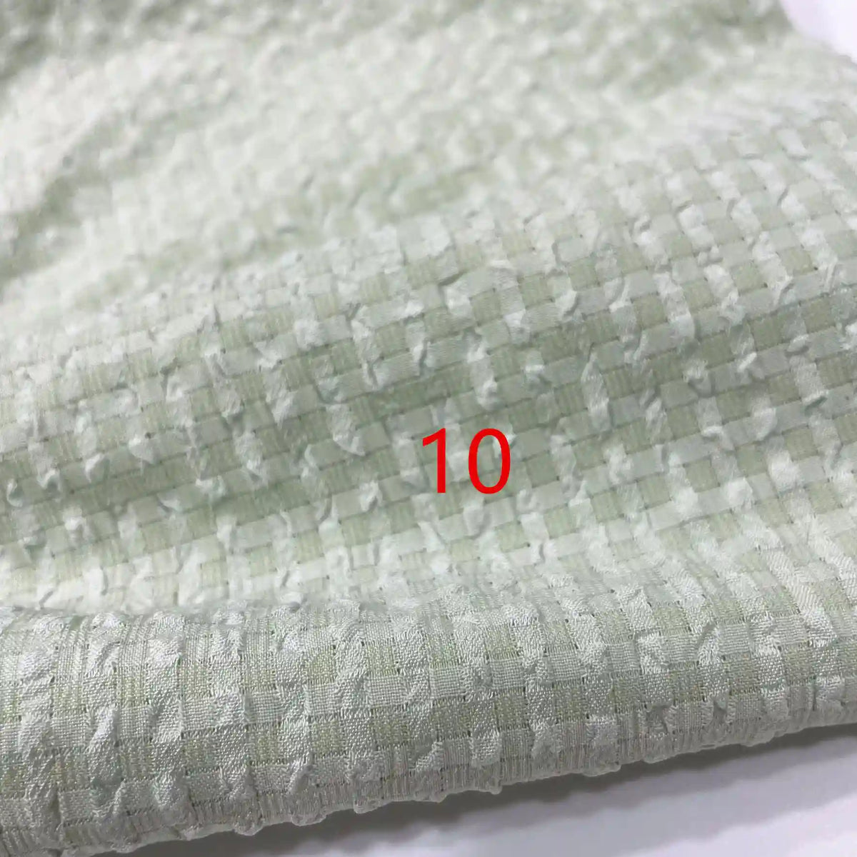 Un gros plan du polyester Seersucker à carreaux vichy au mètre de Longan Craft France met en évidence sa surface texturée et quadrillée. Le chiffre 10 apparaît en rouge au centre de l'image.