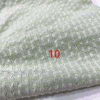 Un gros plan du polyester Seersucker à carreaux vichy au mètre de Longan Craft France met en évidence sa surface texturée et quadrillée. Le chiffre 10 apparaît en rouge au centre de l'image.