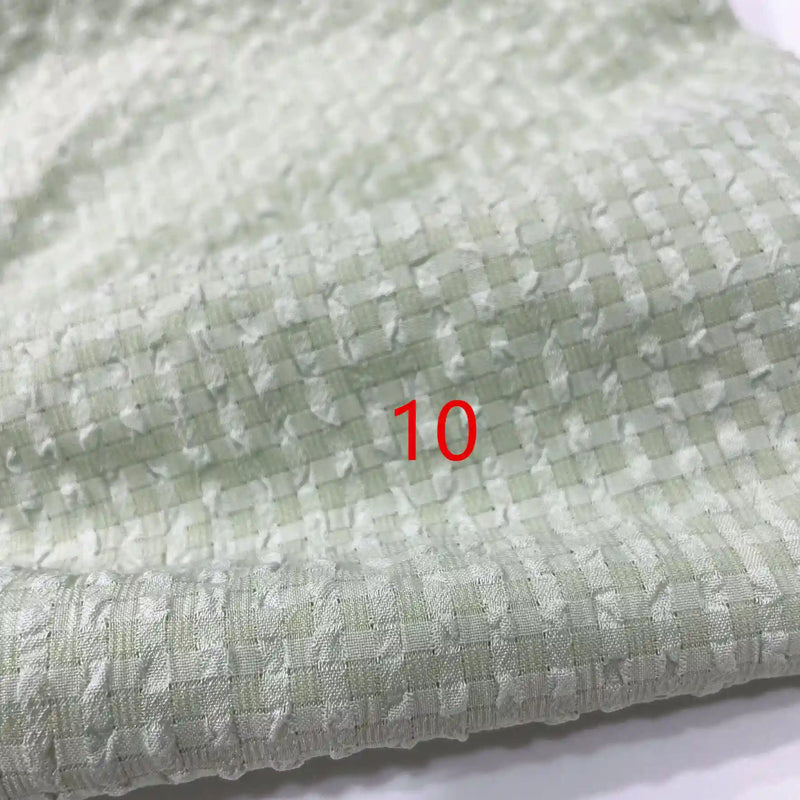 Un gros plan du polyester Seersucker à carreaux vichy au mètre de Longan Craft France met en évidence sa surface texturée et quadrillée. Le chiffre 10 apparaît en rouge au centre de l'image.