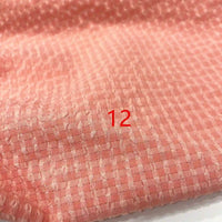 Gros plan sur le Seersucker polyester à carreaux vichy au mètre de Longan Craft France, montrant un tissu à carreaux rose froissé. Le numéro 12 rouge est imprimé au centre.