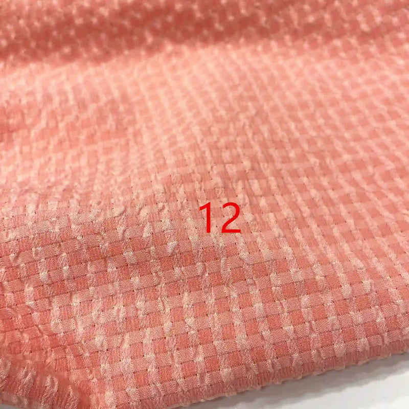 Gros plan sur le Seersucker polyester à carreaux vichy au mètre de Longan Craft France, montrant un tissu à carreaux rose froissé. Le numéro 12 rouge est imprimé au centre.