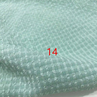 Un gros plan de Seersucker polyester à carreaux vichy au mètre de Longan Craft France montre un tissu seersucker polyester vert clair, froissé, avec une petite grille carrée ; le nombre 14 apparaît en rouge près du centre.