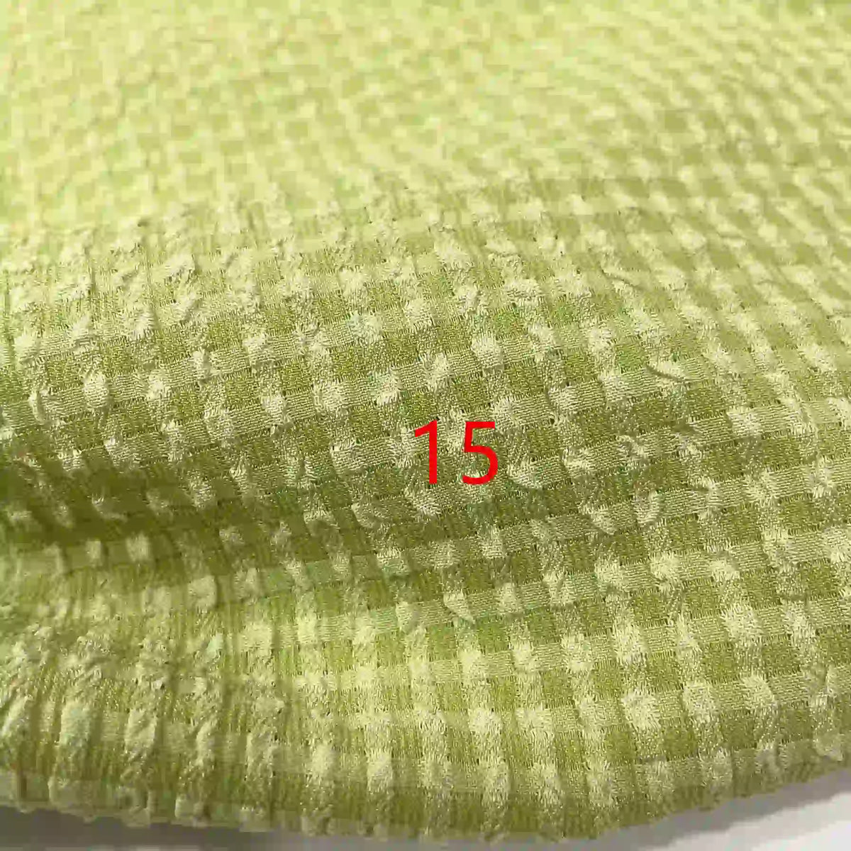 Gros plan sur le polyester seersucker à carreaux vichy de Longan Craft France, vert clair avec un motif à petits carreaux. Le numéro 15 est centré en texte rouge sur le tissu froissé.