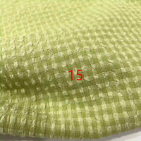 Gros plan sur le polyester seersucker à carreaux vichy de Longan Craft France, vert clair avec un motif à petits carreaux. Le numéro 15 est centré en texte rouge sur le tissu froissé.