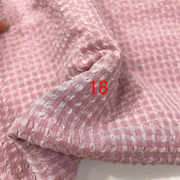 Un gros plan du polyester Seersucker à carreaux vichy au mètre de Longan Craft France montre son motif rose clair, texturé et quadrillé. Le chiffre 18 est superposé en rouge près du centre de l'image.