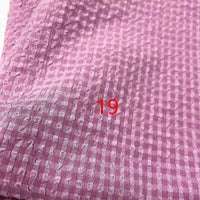 Le Seersucker polyester à carreaux vichy au mètre de Longan Craft France est un tissu rose texturé et froissé avec un motif en grille. Le chiffre "19" apparaît en rouge au centre de l'image.