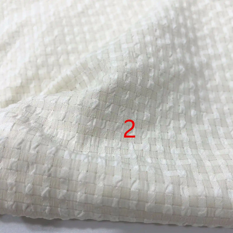 Gros plan sur le polyester Seersucker à carreaux vichy au mètre de Longan Craft France, montrant son motif de grille froissée avec un numéro 2 rouge imprimé sur le tissu.