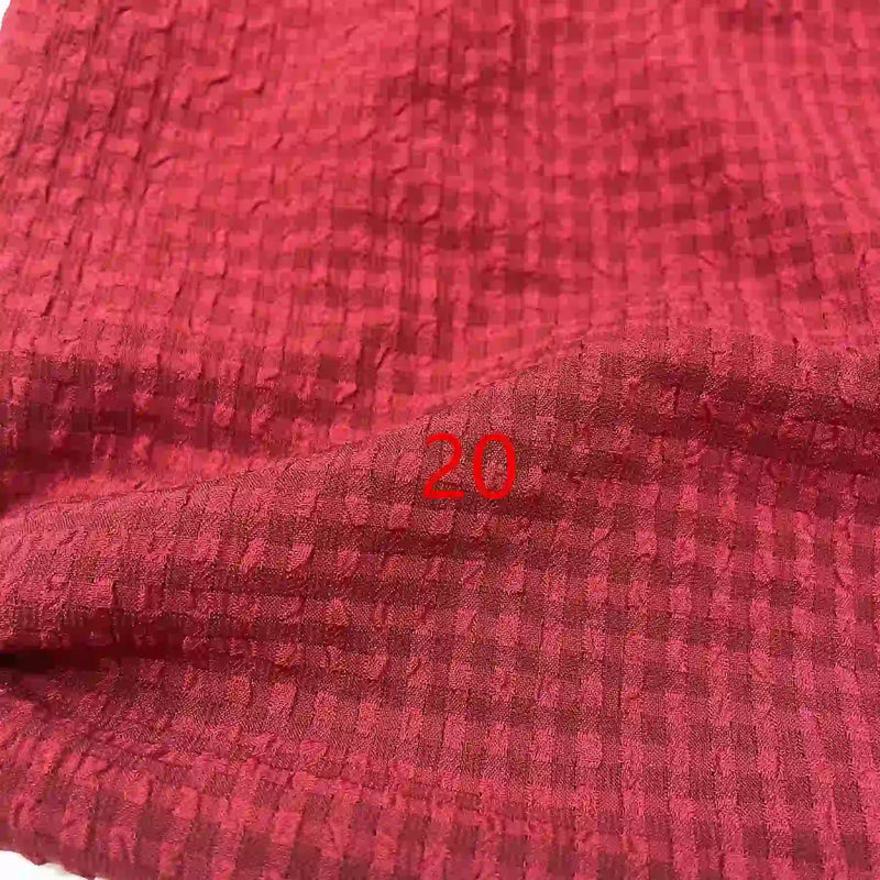 Un gros plan du Seersucker polyester à carreaux vichy au mètre de Longan Craft France montre un tissu texturé rouge froissé avec un motif à carreaux subtil et le nombre "20" imprimé en rouge au centre.