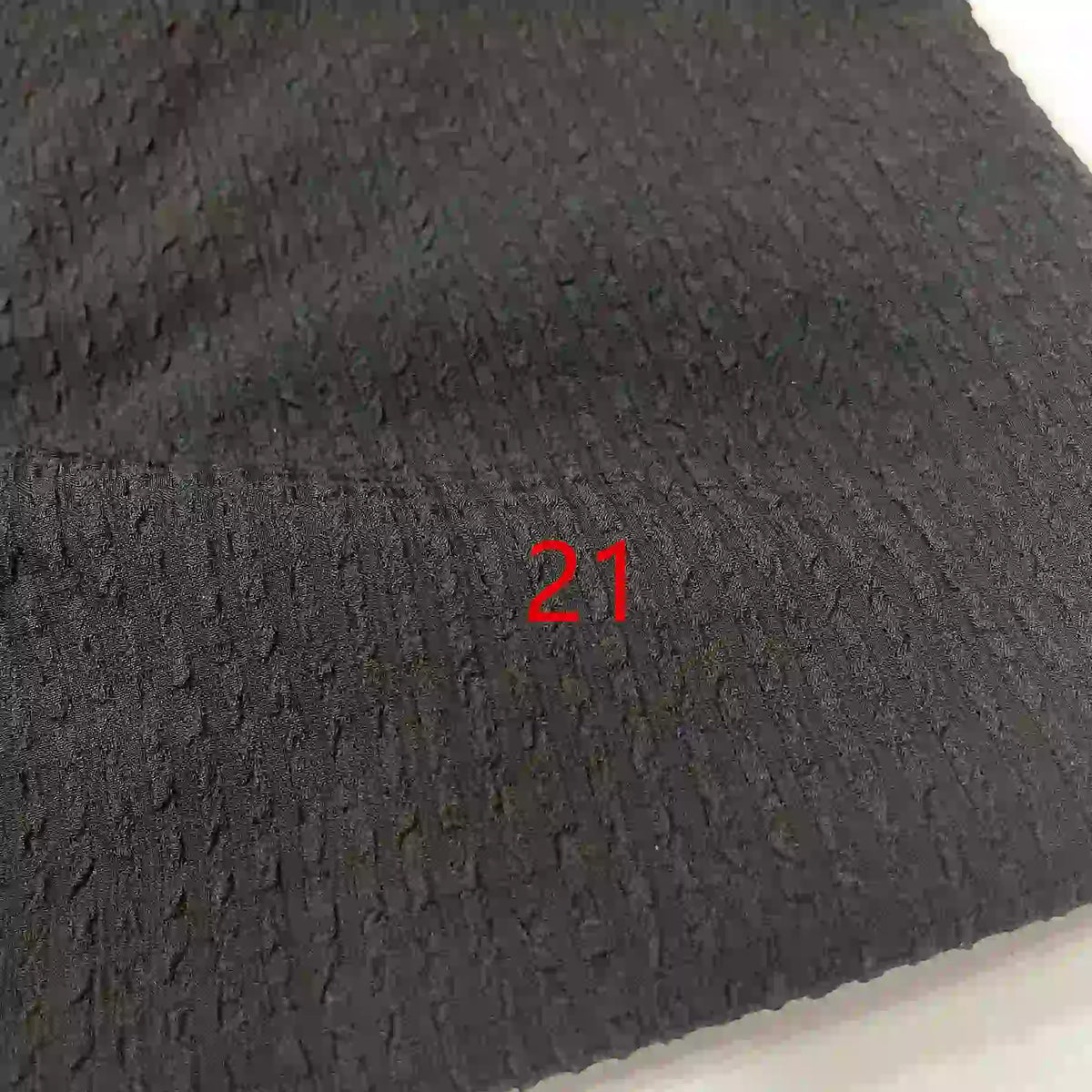 Un gros plan du Seersucker polyester à carreaux vichy au mètre de Longan Craft France montre sa surface texturée en seersucker noir avec un numéro 21 rouge imprimé au centre.