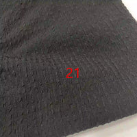 Un gros plan du Seersucker polyester à carreaux vichy au mètre de Longan Craft France montre sa surface texturée en seersucker noir avec un numéro 21 rouge imprimé au centre.