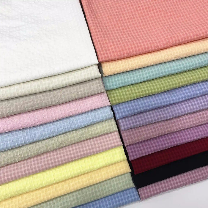 Les échantillons de polyester seersucker à carreaux vichy de Longan Craft France, soigneusement empilés et à la texture gaufrée, présentent une gamme de couleurs allant du blanc au noir, en passant par des teintes vives comme le rose, le jaune et le vert.