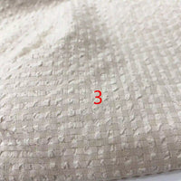 Gros plan sur le tissu seersucker en polyester à carreaux vichy de Longan Craft France, montrant sa texture froissée et ses carreaux subtils, avec un numéro 3 rouge centré sur l'image.