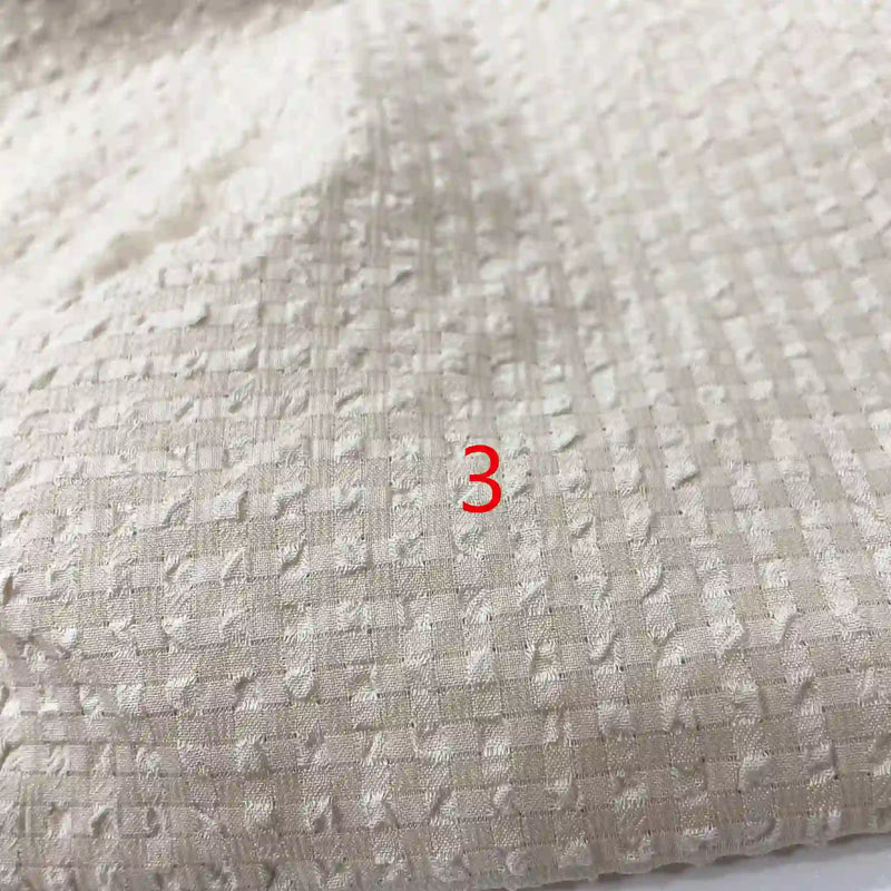Gros plan sur le tissu seersucker en polyester à carreaux vichy de Longan Craft France, montrant sa texture froissée et ses carreaux subtils, avec un numéro 3 rouge centré sur l'image.