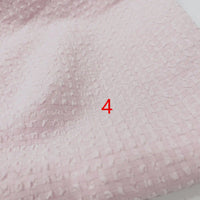 Gros plan sur le polyester Seersucker à carreaux vichy au mètre de Longan Craft France, montrant un tissu rose pâle froissé avec un motif carré tissé et un numéro 4 rouge imprimé près du centre.