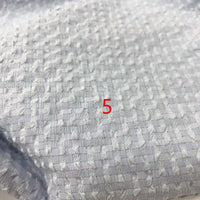 Un gros plan du polyester seersucker à carreaux vichy de Longan Craft France montre un motif de grille carrée sur un tissu texturé gris clair, avec un numéro 5 rouge centré sur le tissu froissé.