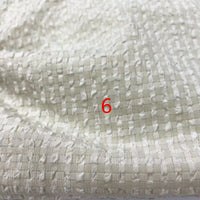 Gros plan sur le seersucker polyester à carreaux vichy au mètre de Longan Craft France, un tissu seersucker texturé blanc cassé avec un motif carré en relief. Le numéro 6 rouge est centré sur le tissu léger froissé.