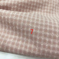 Un gros plan du polyester seersucker à carreaux vichy de Longan Craft France montre un tissu texturé rose clair et blanc avec un numéro 7 rouge centré.
