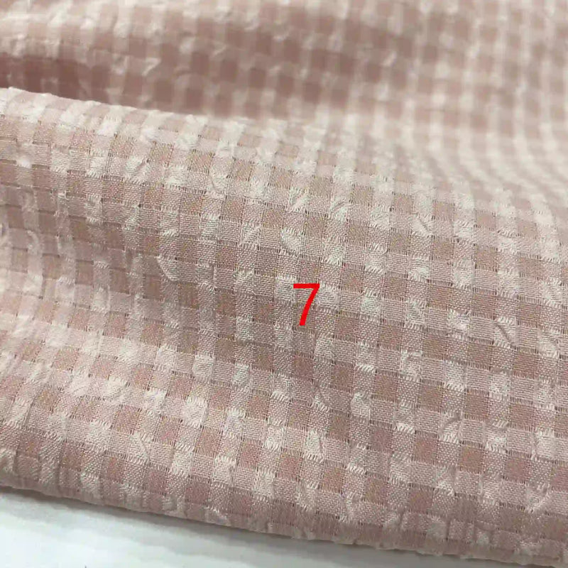 Un gros plan du polyester seersucker à carreaux vichy de Longan Craft France montre un tissu texturé rose clair et blanc avec un numéro 7 rouge centré.