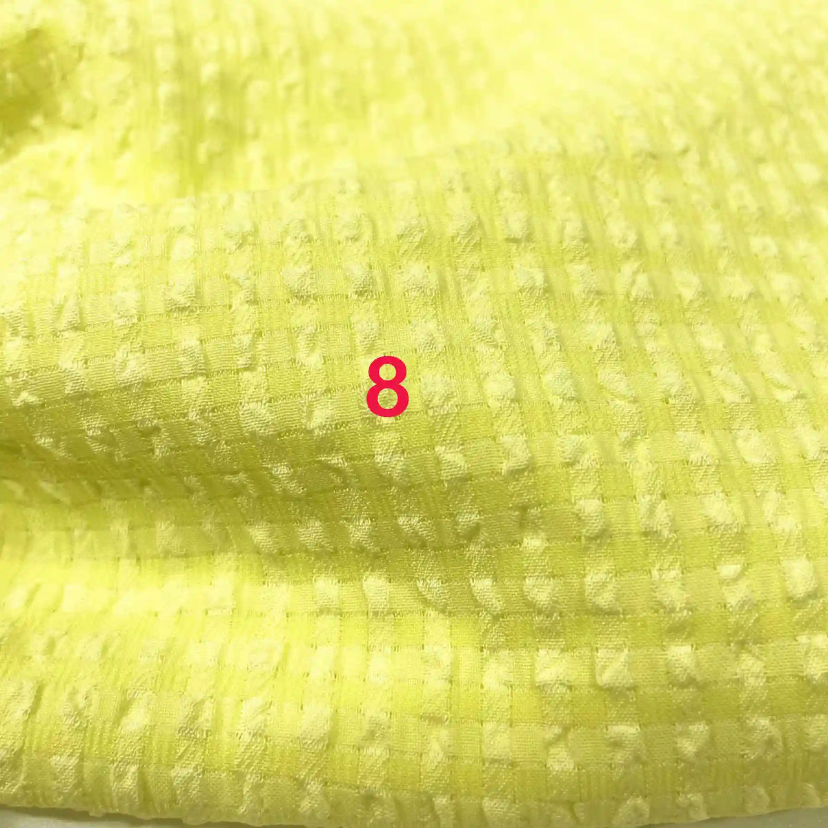 Un gros plan du tissu Longan Craft France seersucker polyester à carreaux vichy montre un motif à carreaux jaune texturé avec le chiffre 8 en police rose vif centré sur lui.