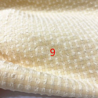 Un gros plan du polyester seersucker à carreaux vichy au mètre de Longan Craft France montre un motif à carreaux beige et texturé avec un numéro 9 rouge imprimé au centre.