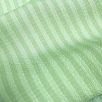 Gros plan sur le Seersucker à larges rayures au mètre de Longan Craft France : polyester seersucker vert clair avec des rayures verticales plus foncées régulièrement espacées et une brillance subtile - idéal pour la décoration intérieure ou les chemises vintage.