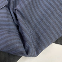 Un gros plan du Seersucker à larges rayures au mètre de Longan Craft France montre un polyester doux et léger avec de fines rayures gris-bleu clair et foncé, délicatement pliées - idéal pour la décoration intérieure ou les chemises vintage.