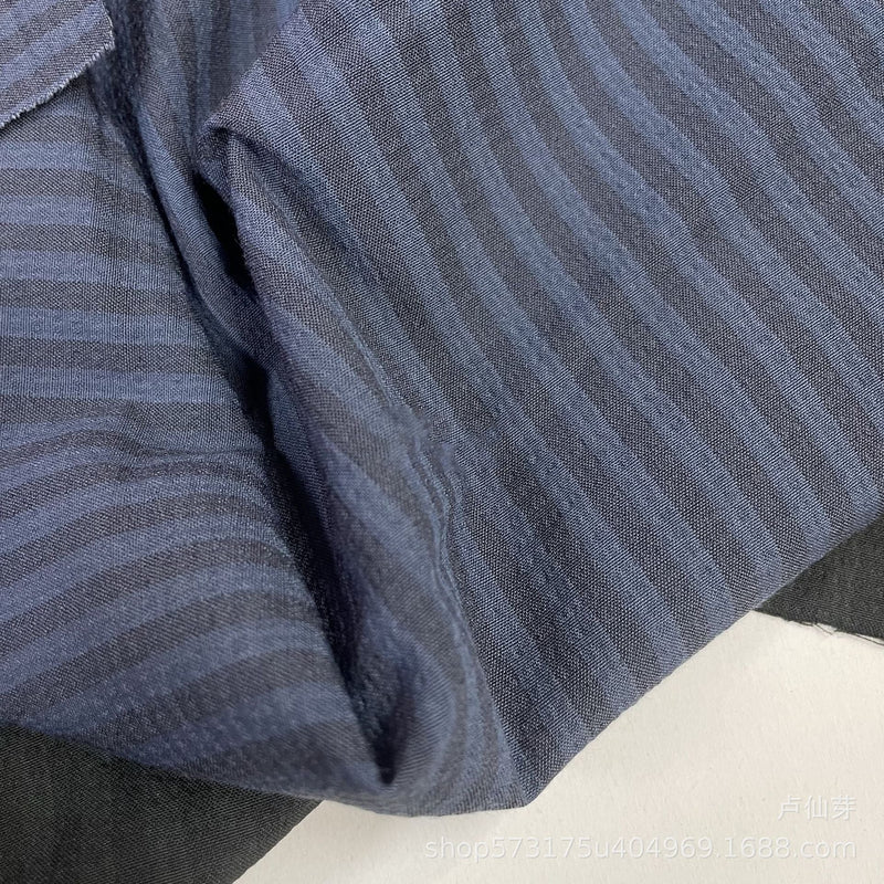 Un gros plan du Seersucker à larges rayures au mètre de Longan Craft France montre un polyester doux et léger avec de fines rayures gris-bleu clair et foncé, délicatement pliées - idéal pour la décoration intérieure ou les chemises vintage.