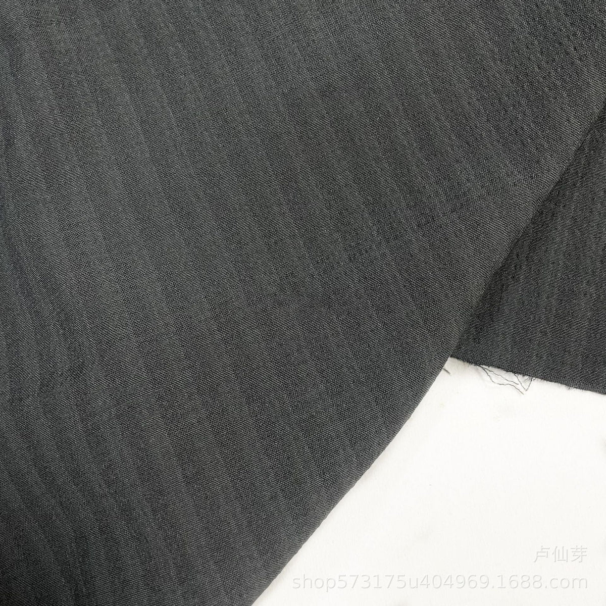 Un gros plan de Seersucker à larges rayures au mètre de Longan Craft France montre un tissu de polyester seersucker gris foncé subtilement rayé pour chemises, posé à plat sur du blanc avec des bords visibles et une petite section effilochée.
