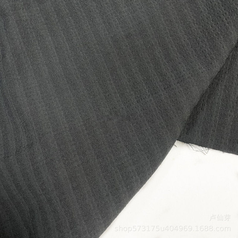 Un gros plan de Seersucker à larges rayures au mètre de Longan Craft France montre un tissu de polyester seersucker gris foncé subtilement rayé pour chemises, posé à plat sur du blanc avec des bords visibles et une petite section effilochée.