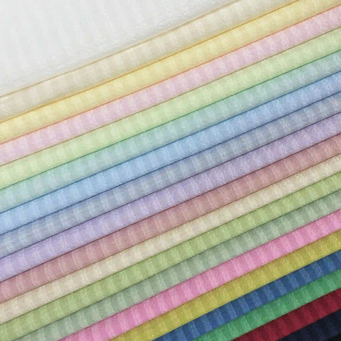 Les feuilles de tissu Seersucker en polyester arc-en-ciel de Longan Craft France, empilées avec soin, vont du blanc et du jaune aux bleus et rouges profonds, mettant en valeur la texture légère et vintage idéale pour les chemises.