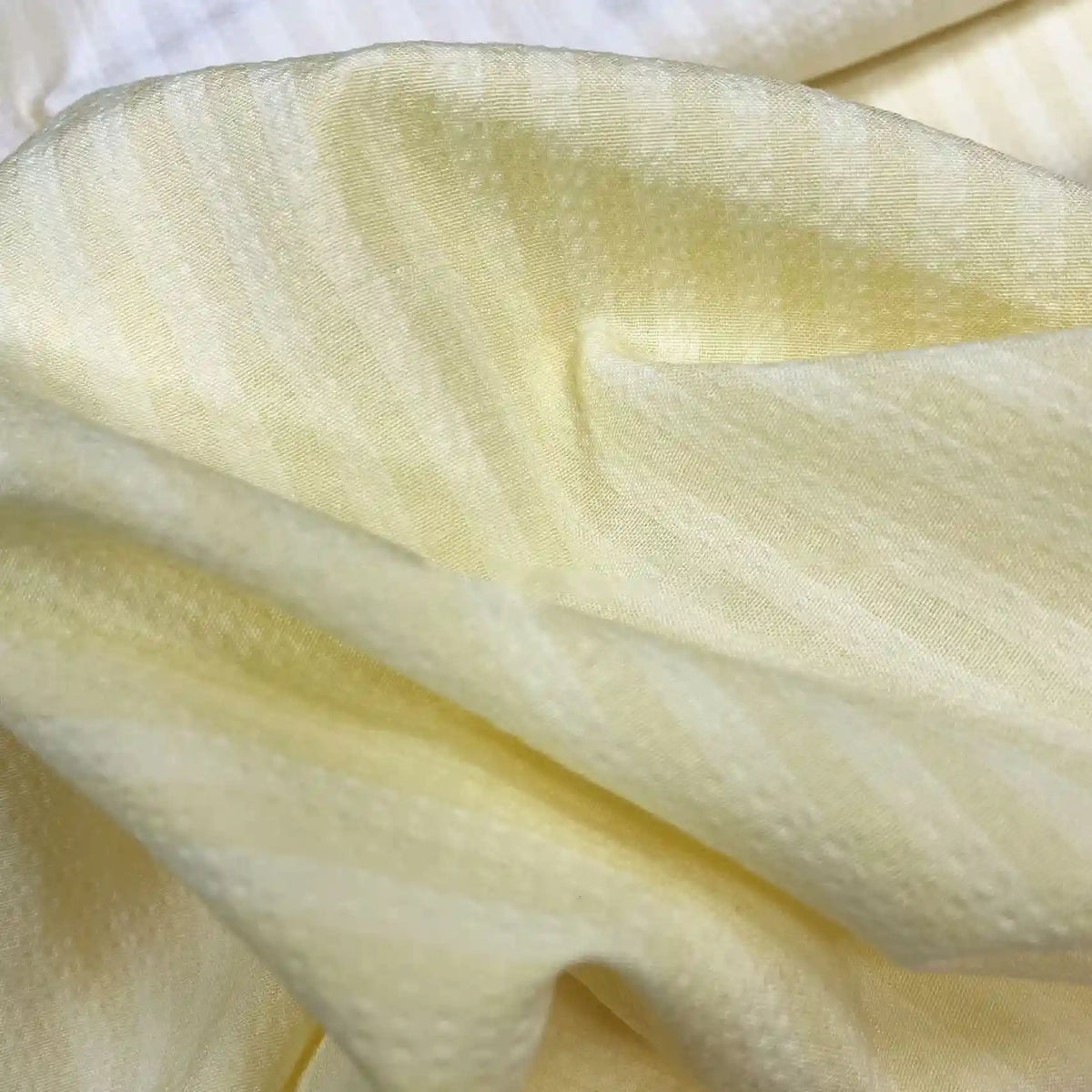 Gros plan sur le Seersucker à larges rayures au mètre de Longan Craft France : seersucker de polyester jaune clair de style vintage avec des rayures subtiles et une surface texturée - parfait pour les chemises ou la décoration intérieure.