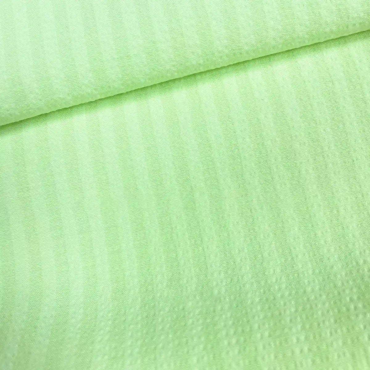Un gros plan du Seersucker à larges rayures au mètre de Longan Craft France montre son polyester vert clair avec de subtiles rayures verticales et une surface douce et texturée, légèrement pliée vers le haut. Idéal pour les chemises de style vintage.