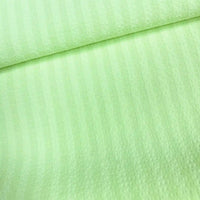 Un gros plan du Seersucker à larges rayures au mètre de Longan Craft France montre son polyester vert clair avec de subtiles rayures verticales et une surface douce et texturée, légèrement pliée vers le haut. Idéal pour les chemises de style vintage.