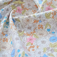 Un gros plan sur le tissu popeline de coton imprimé au mètre de Longan Craft France révèle un tissu floral doux et plié 100 % coton en blanc, rose, bleu, jaune, vert et orange - parfait pour le quilting DIY, les langes, les peignoirs et les chemises.