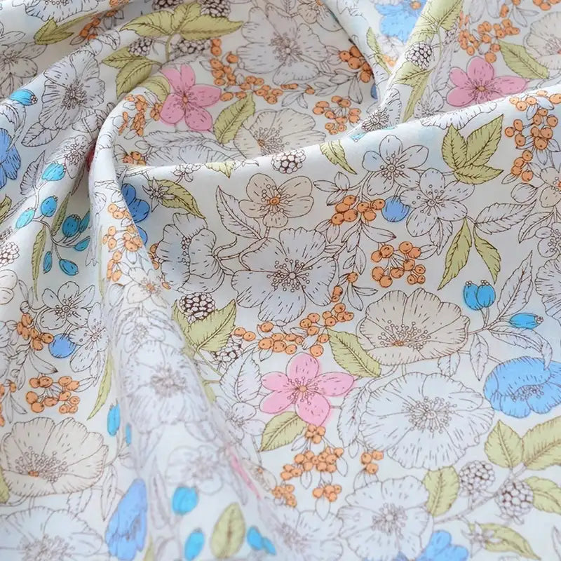 Un gros plan sur le tissu popeline de coton imprimé au mètre de Longan Craft France révèle un tissu floral doux et plié 100 % coton en blanc, rose, bleu, jaune, vert et orange - parfait pour le quilting DIY, les langes, les peignoirs et les chemises.