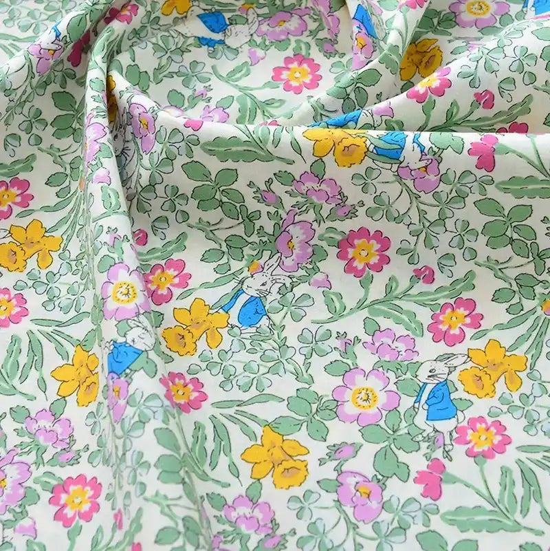 Découvrez le tissu popeline de coton imprimé au mètre, unie 40S 100% coton, à motifs floraux roses, jaunes et verts avec petits lapins bleus. Idéal pour DIY, quilting, nappes, robes et chemises.
