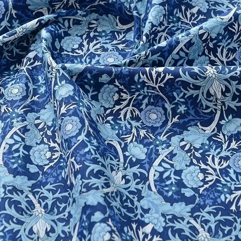 Un gros plan du Tissu popeline de coton imprimé au mètre de Longan Craft France révèle un motif floral bleu et blanc détaillé. Le tissu 100% coton légèrement froissé ajoute une texture riche, parfaite pour le bricolage, le quilting, les peignoirs, les chemises et les langes.