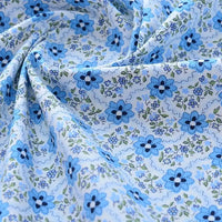Gros plan sur le tissu popeline de coton imprimé au mètre de Longan Craft France, 100% coton à motifs floraux bleus et verts sur fond bleu clair, légèrement froissé et idéal pour DIY, quilting, nappes, robes ou chemises.