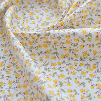 Gros plan sur le Tissu popeline de coton imprimé au mètre de Longan Craft France, 100% coton avec des motifs floraux - parfait pour le bricolage, le quilting, les nappes, les robes et les chemises. Légèrement froncé, avec des plis visibles et des fleurs jaunes.