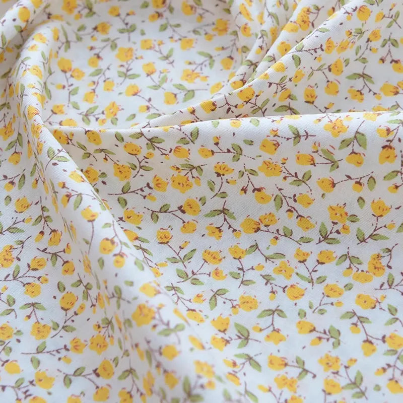 Gros plan sur le Tissu popeline de coton imprimé au mètre de Longan Craft France, 100% coton avec des motifs floraux - parfait pour le bricolage, le quilting, les nappes, les robes et les chemises. Légèrement froncé, avec des plis visibles et des fleurs jaunes.