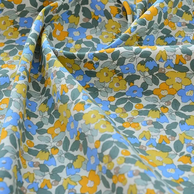 Le tissu popeline de coton imprimé au mètre Longan Craft France présente des motifs floraux jaunes, bleus et orange avec feuillage vert sur fond clair, idéal pour DIY, quilting, nappes, robes ou chemises.