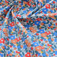 Gros plan sur le Tissu popeline de coton imprimé au mètre par Longan Craft France, un tissu floral 100% coton avec motifs colorés rouges, bleus, orange et jaunes sur fond clair, délicatement plissé en douces ondulations.