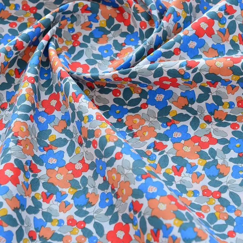 Gros plan sur le Tissu popeline de coton imprimé au mètre par Longan Craft France, un tissu floral 100% coton avec motifs colorés rouges, bleus, orange et jaunes sur fond clair, délicatement plissé en douces ondulations.