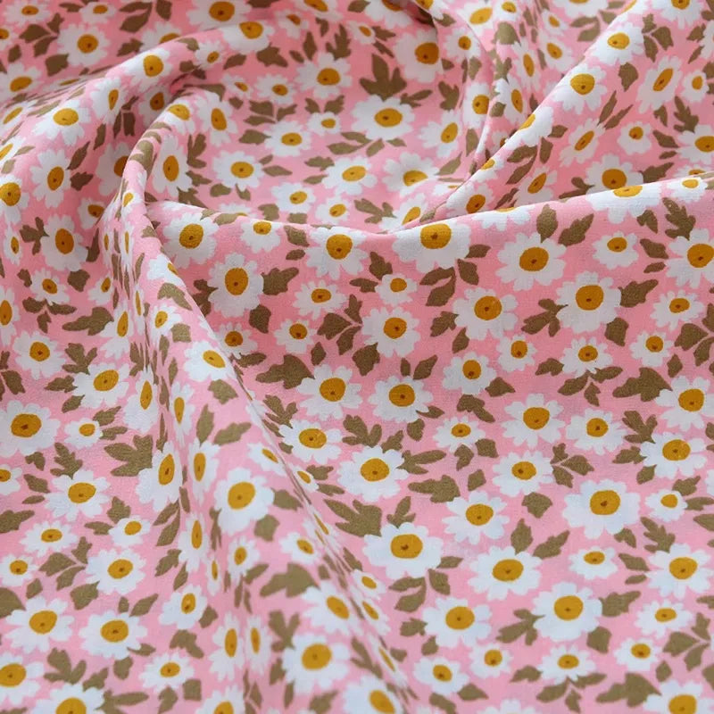 Un gros plan de Longan Craft France Tissu popeline de coton imprimé au mètre, 100% coton à motifs floraux roses, blancs et jaunes avec feuilles vertes. Légèrement froissé, idéal pour DIY, quilting, nappes, robes et chemises.