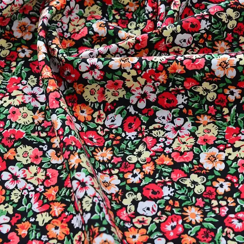 Gros plan sur le Tissu popeline de coton imprimé au mètre de Longan Craft France, 100% coton avec des motifs floraux denses rouges, jaunes, orange et blancs sur fond noir - légèrement froissé, parfait pour le bricolage, le quilting, les langes, les peignoirs et les chemises.