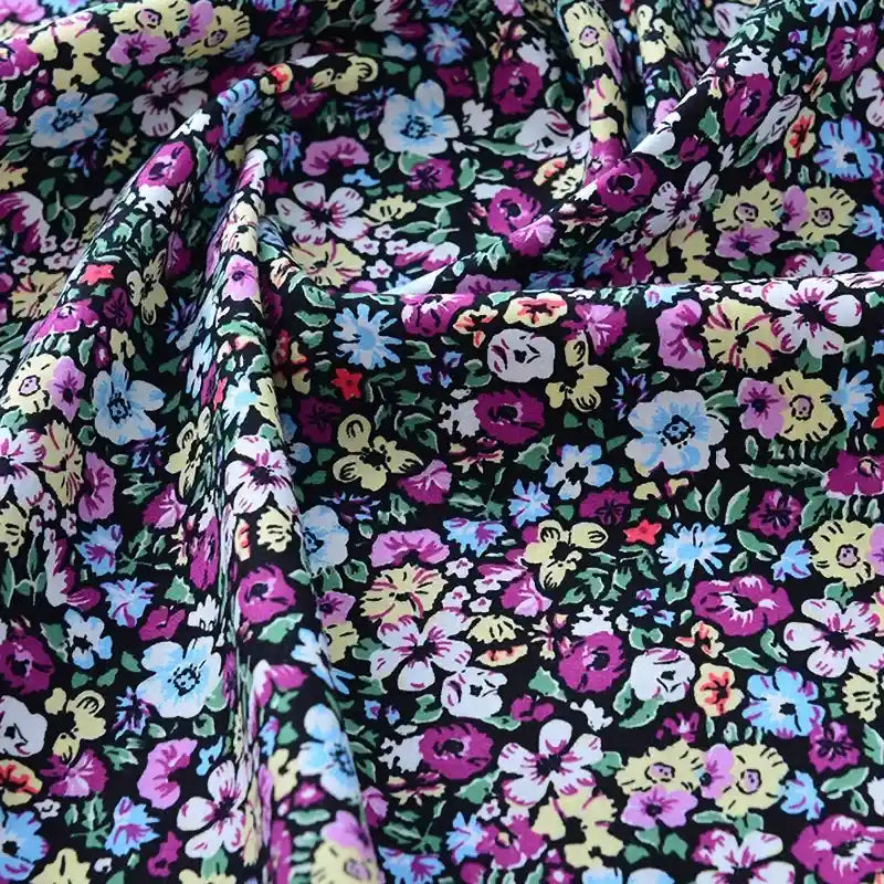 Gros plan sur le tissu popeline de coton imprimé au mètre de Longan Craft France, 100% coton, à motifs floraux colorés sur fond noir, légèrement froissé et drapé, idéal pour DIY, quilting, nappes, robes et chemises.