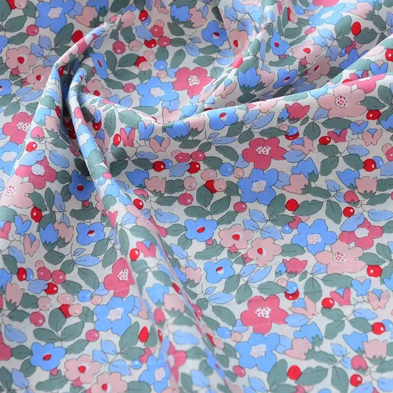 Un gros plan de Longan Craft France Tissu popeline de coton imprimé au mètre, 100% coton 40S à motifs floraux colorés sur fond clair, idéal pour DIY, quilting, nappes, robes et chemises. Sa texture légèrement froissée met en valeur son drapé élégant.