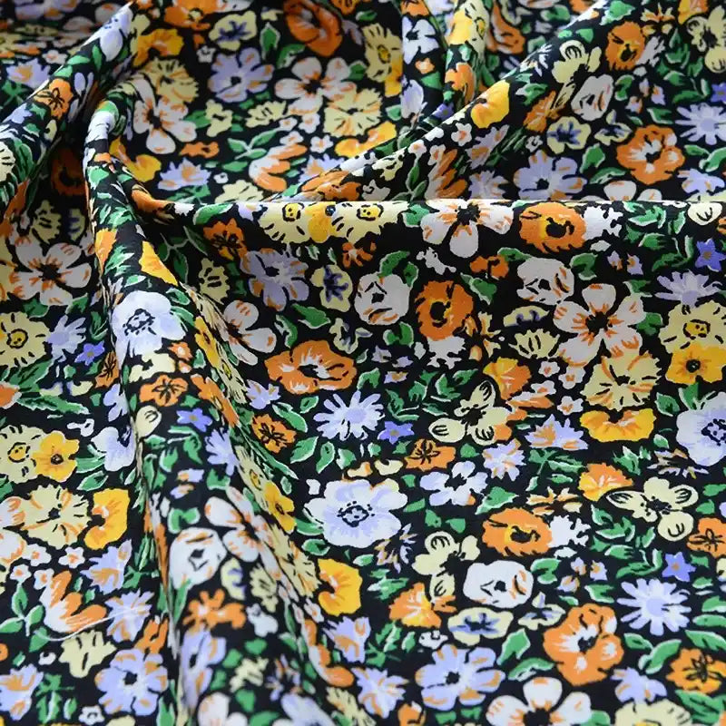 Gros plan sur le Tissu popeline de coton imprimé au mètre de Longan Craft France, qui présente un motif floral vibrant - fleurs jaunes, blanches, orange et violet clair sur fond noir - idéal pour le bricolage, le quilting, les langes, les peignoirs et les chemises. Légèrement froissé pour plus de texture.